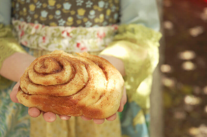 Little girl holding a giant cinnamon roll in her hands.