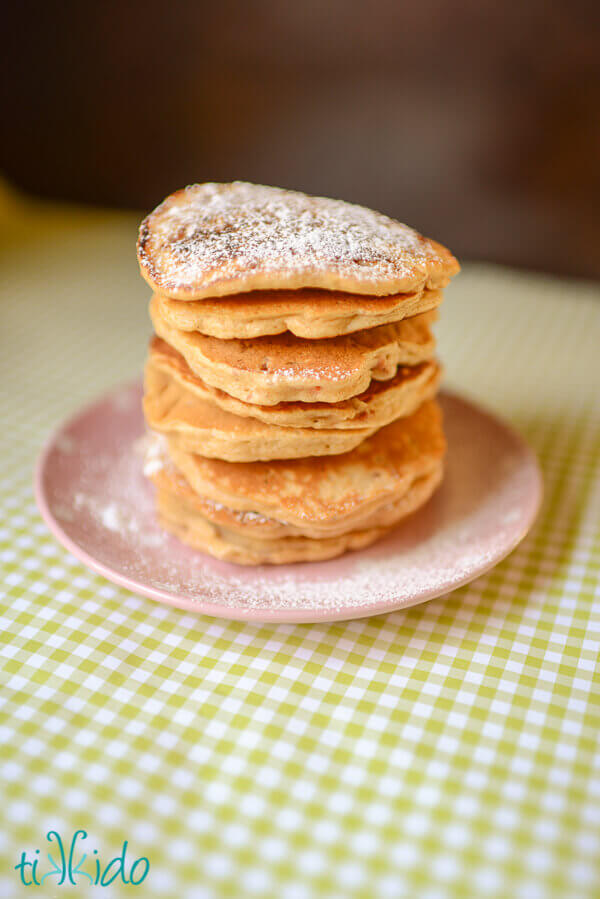 Stack of carrot cake pancakes dusted with powdered sugar on a pink and white polka dot plate.