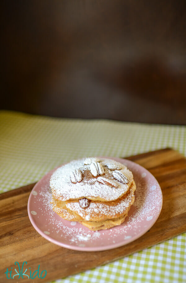 Stack of carrot cake pancakes dusted with powdered sugar on a pink and white polka dot plate.