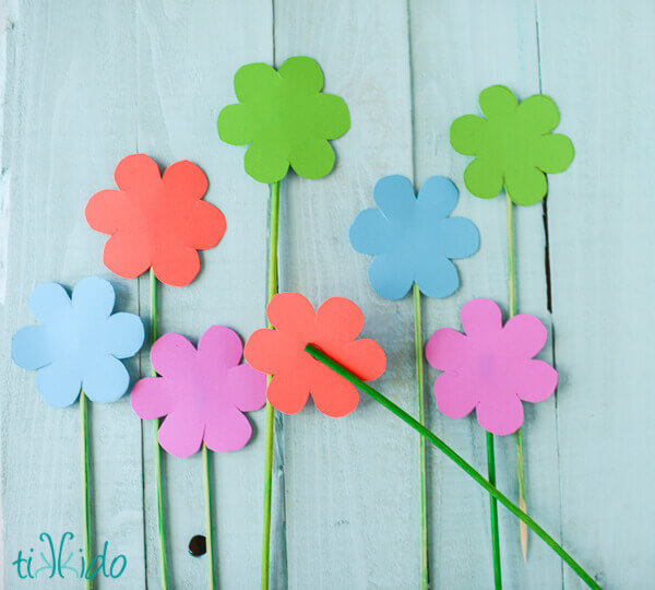 Cardstock cut out flowers on green bamboo skewers.