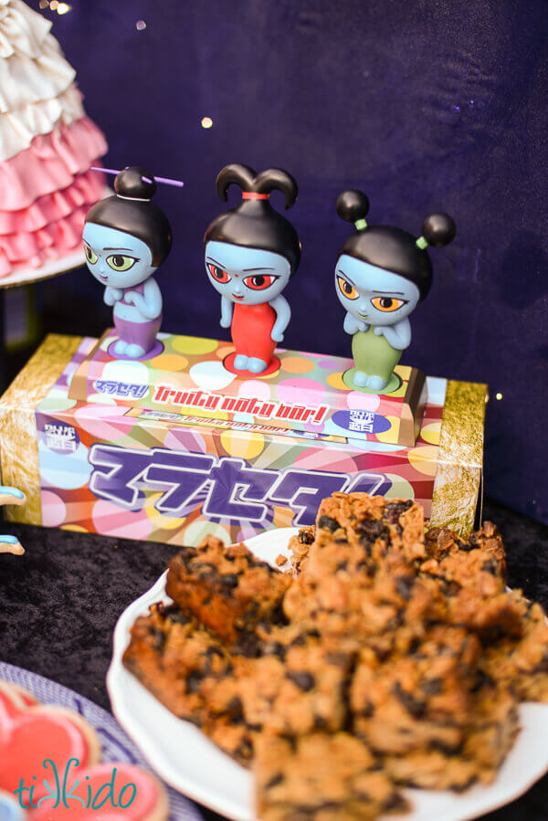 Firefly Fruity Oaty Bars on a white plate in front of figurines of the fruity oaty bars mascots from the Firefly movie.