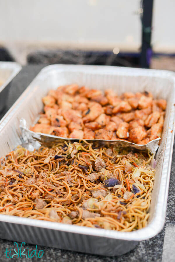 Foil caterer's tray filled with pancit canton and orange chicken.