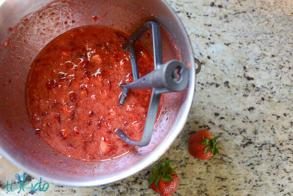 Strawberry freezer jam ingredients mixed together in a kitchenaid mixer bowl on granite counter.
