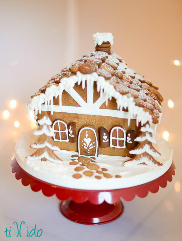 Chalet gingerbread house decorated entirely in royal icing, on a red cake plate.