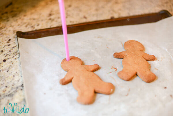 Holes being poked in baked gingerbread men to turn them into Christmas ornaments.