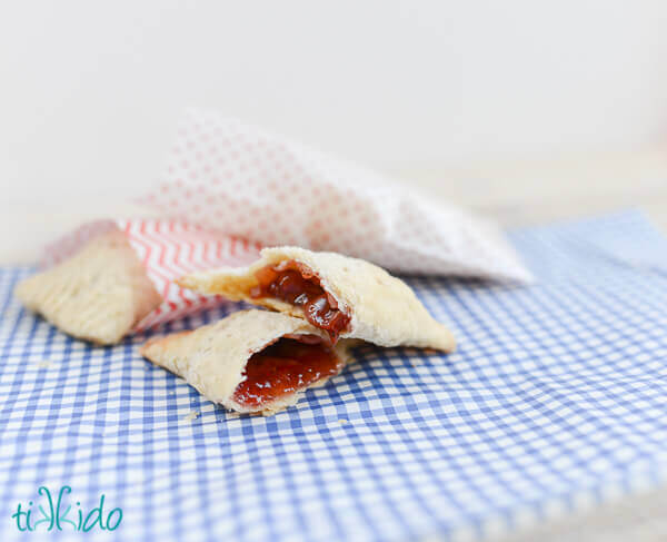 Cherry hand pies, one broken in half so you can see the filling, on a blue gingham surface.
