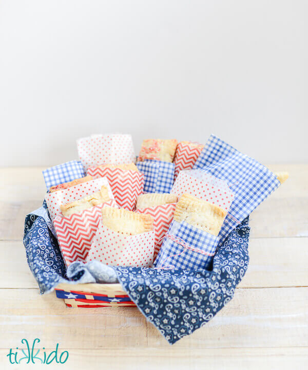 Homemade hand pies wrapped in red, white, and blue waxed paper, arranged in a basket.