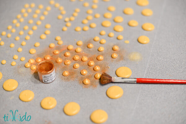 Round royal icing dots on waxed paper, being brushed with gold luster dust.