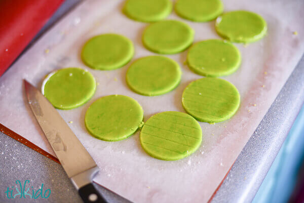 green round sugar cookies on parchment paper lined baking sheet.  Some of the cookies have been scored with perpendicular lines with a sharp knife.