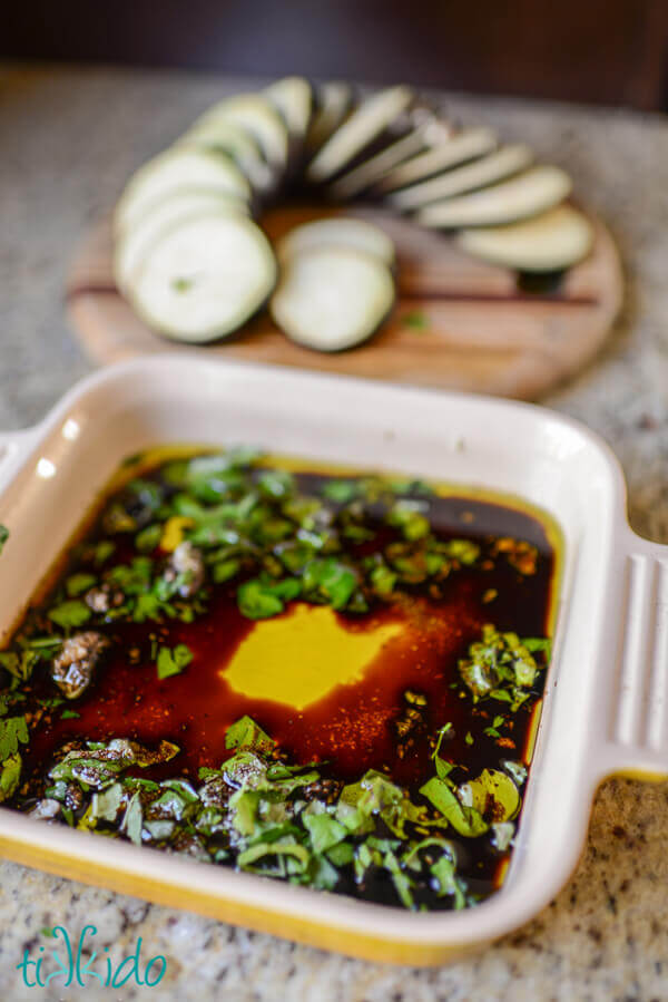 Italian marinade in a square baking dish, cutting board with sliced eggplant behind.