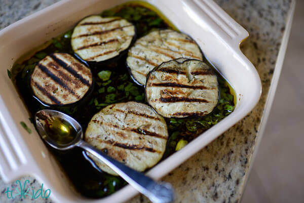 Grilled eggplant antipasto soaking in square baking dish full of Italian marinade.