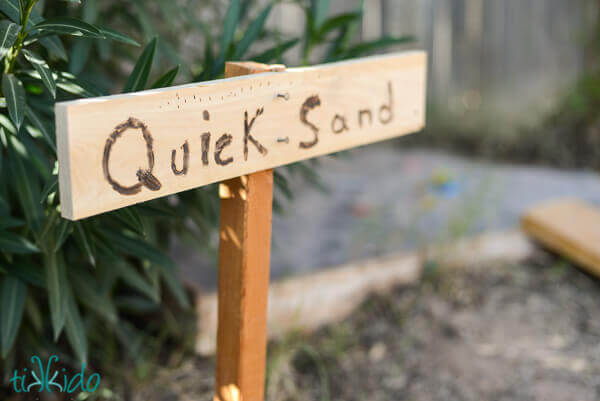 Wooden sign saying "Quick-sand" next to a sandbox activity at a Jungle birthday party.