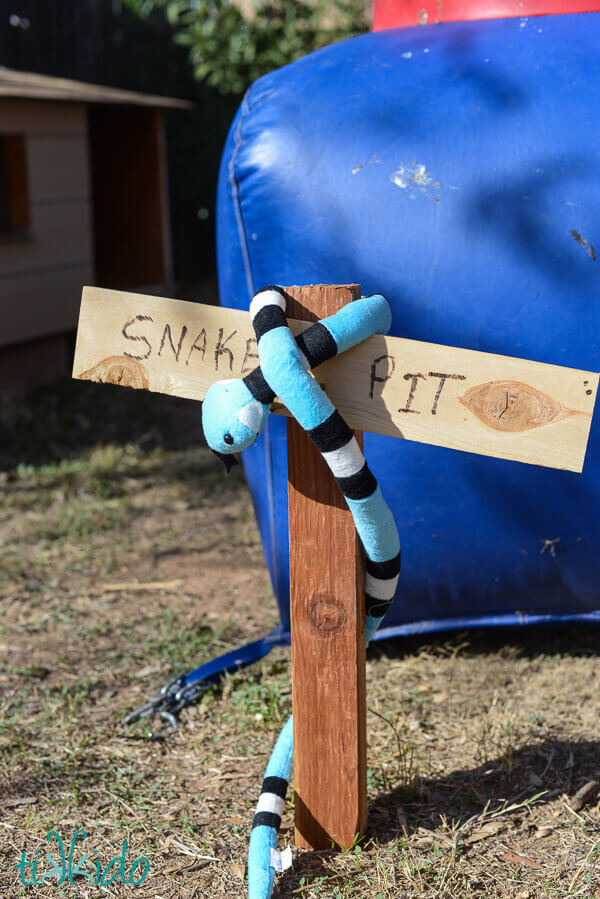 Snake Pit sign next to a bounce house, with a stuffed snake wrapped around the wooden sign.