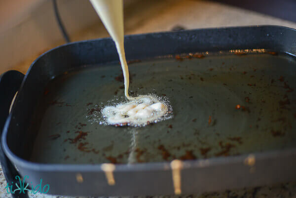 Homemade funnel batter being squeezed from a piping bag into hot oil.