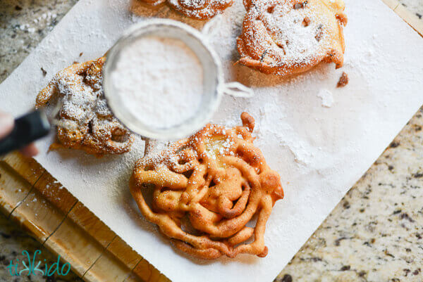 Homemade funnel cakes being dusted with powdered sugar.