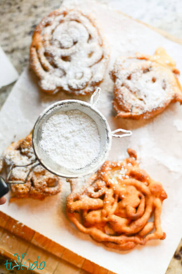 Homemade funnel cakes being dusted with powdered sugar.