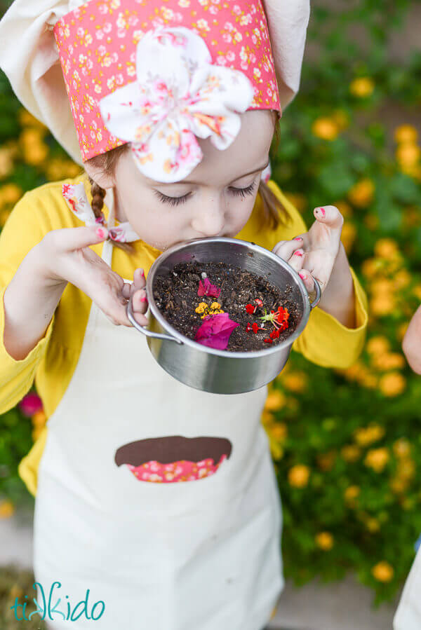 Little girl wearing a chef hat and apron making mud pies.