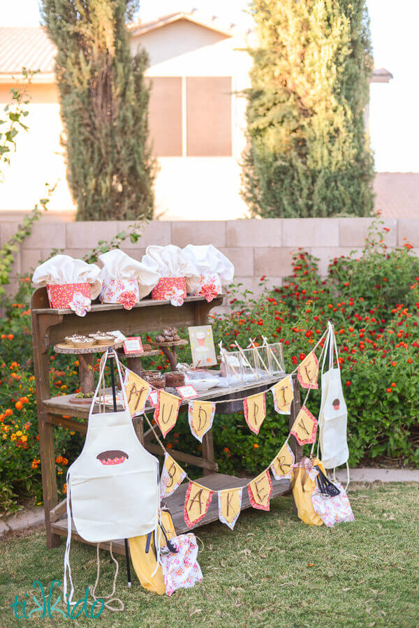 Aprons, party bunting, chef hats, and desserts set up on a wooden potting bench for the Mud Pie Bakery Birthday.