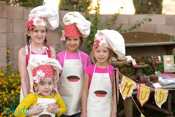 Four girls wearing chef hats and aprons for the mud pie bakery birthday party.
