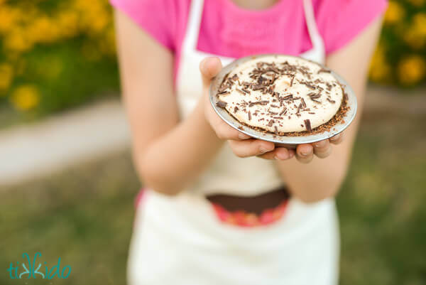 Little girl holding a miniature peanut butter cream pie with chocolate graham cracker crust.