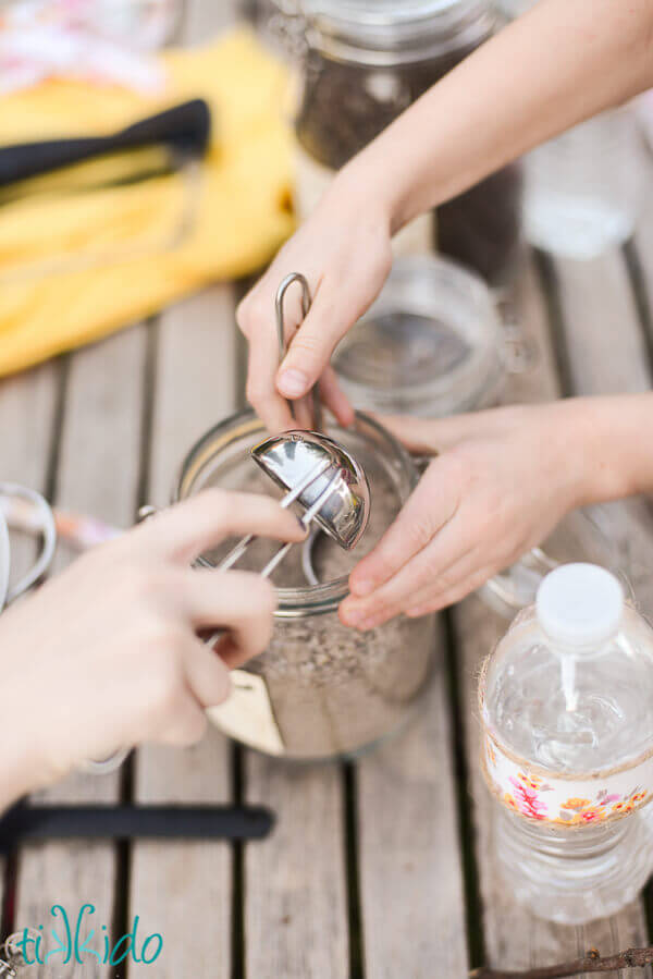 Children's hands scooping out sand from a glass jar to make mud pies.