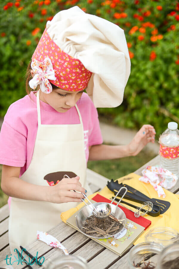 Little girl wearing a chef hat and apron making mud pies.