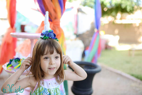 Little girl wearing a felt unicorn headband with  blue felt flowers.