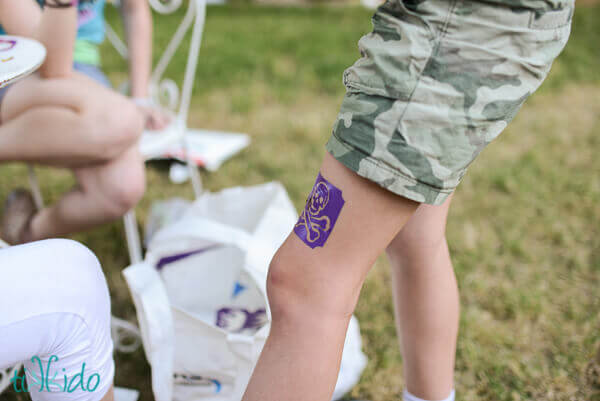 Girl getting a glitter tattoo on her leg.