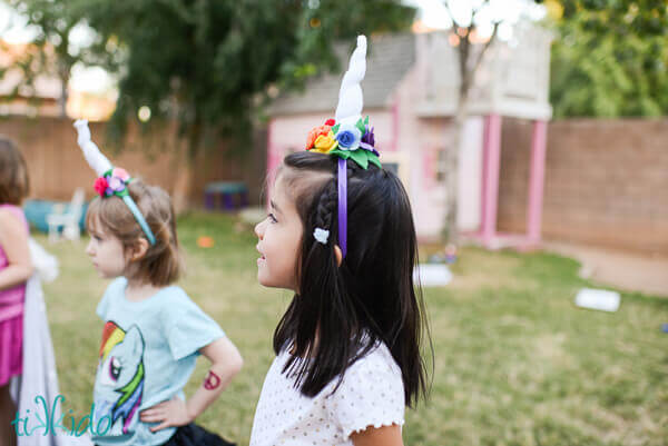 Two young girls at a birthday party wearing felt unicorn horn headbands.
