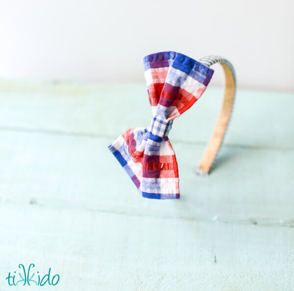 DIY headband made with a no sew fabric bow in red, white, and blue plaid fabric.