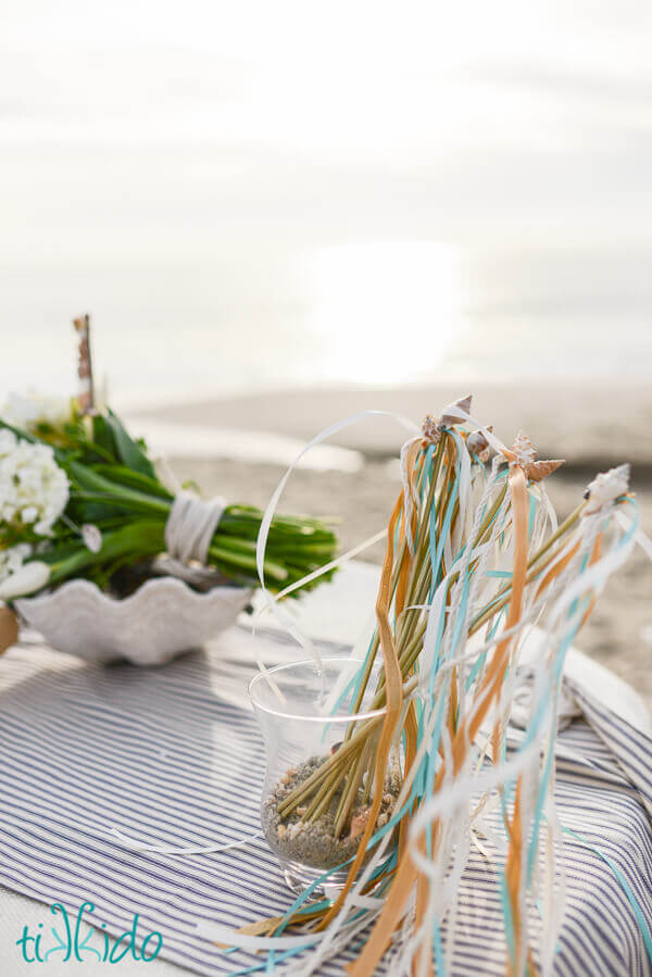 Glass container holding Wedding Ribbon Wands on a table at the beach at sunset.