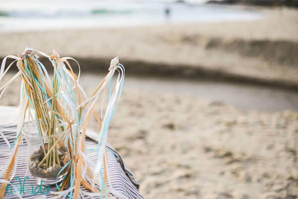 Wedding Ribbon Wands displayed in a glass container on a table at the beach.