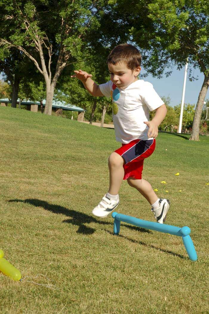 Little boy leaping over hurdles made from balloons in a balloon obstacle course at a balloon birthday party in a park.