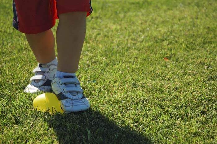 Little boy's feet stomping on a yellow balloon on the grass at the Balloon Themed Birthday Party.