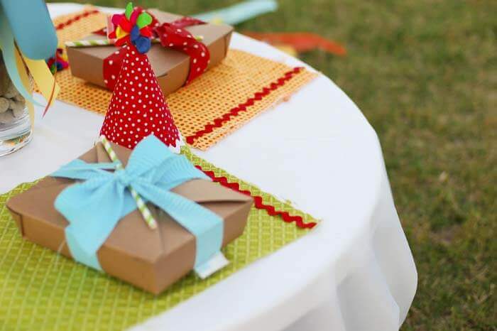 Table settings at a balloon birthday party in the park, with boxed lunches and balloon party hats.