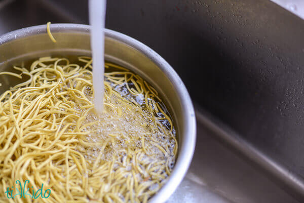 Pancit canton noodles being softened in a bowl of hot water.