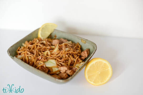 Pancit Canton with pork and pancit noodles in a green bowl, garnished with a lemon wedge.