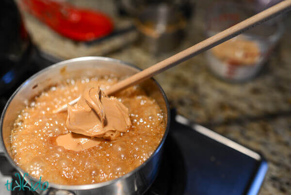 Peanut butter being stirred in to the caramel mixture in a small saucepan.