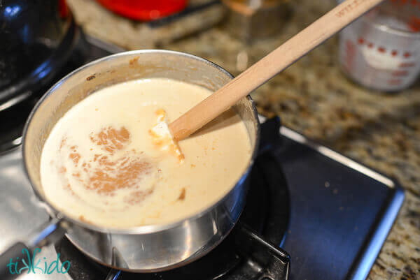Cream being stirred in to the peanut butter caramel mixture in a small saucepan on a gas stove.