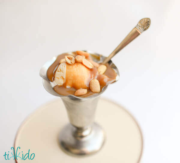 Vanilla ice cream topped with peanuts and peanut butter caramel ice cream topping in a silver ice cream sundae cup on a white background.