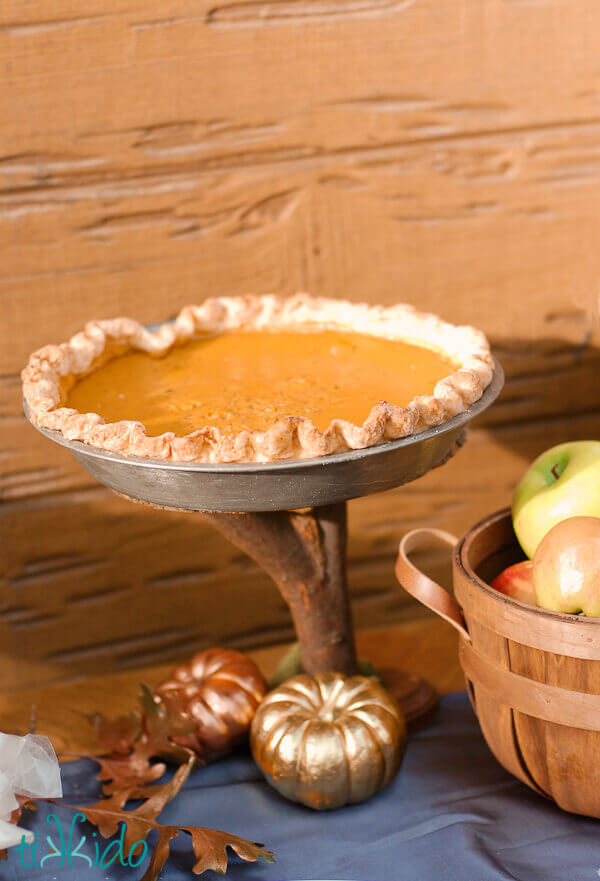 Homemade pumpkin pie on a wooden cake stand.