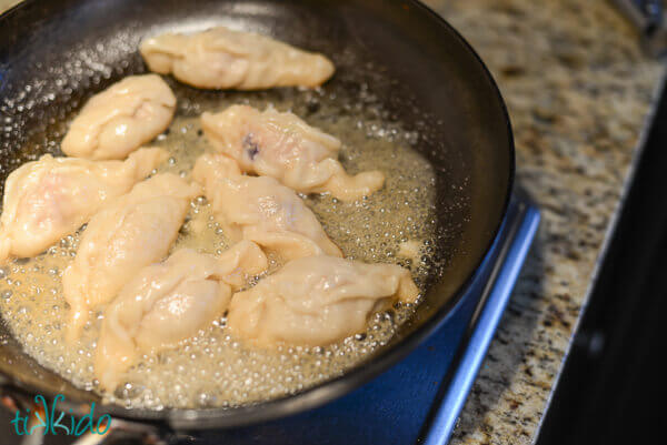 Chinese dumplings being pan fried on the stove.