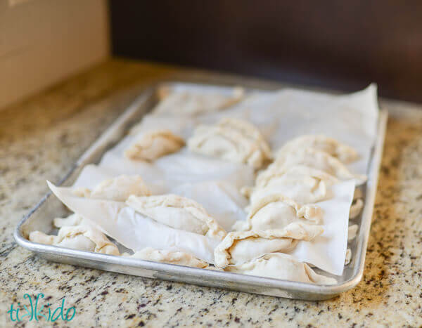 Uncooked pork Chinese dumplings on a baking sheet on a granite counter.