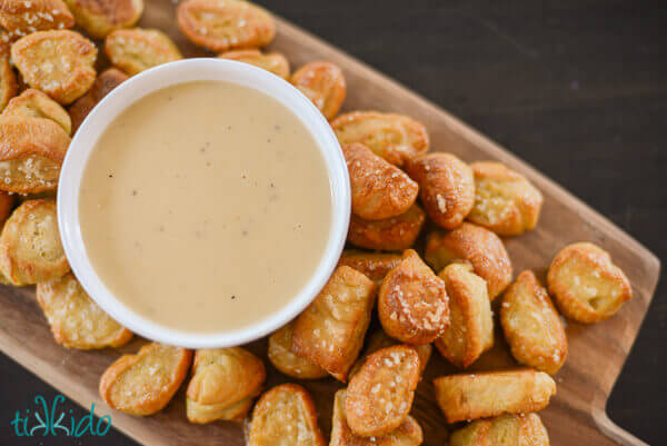 Overhead view of bowl of beer cheddar dipping sauce surrounded by homemade pretzel bites