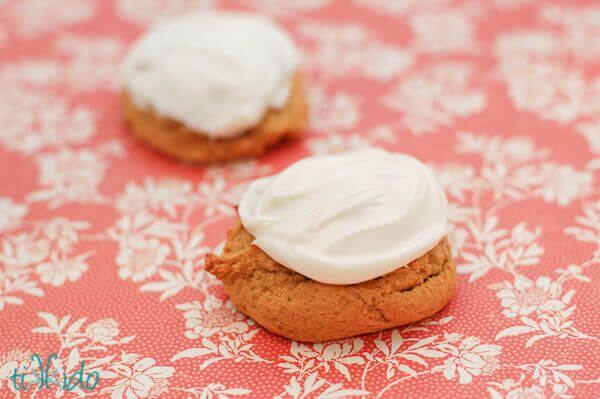 Two pumpkin cookies topped with cream cheese frosting on a floral background..