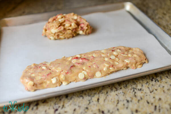 White chocolate strawberry biscotti dough divided in two, and being shaped into two logs on a parchment lined baking sheet.