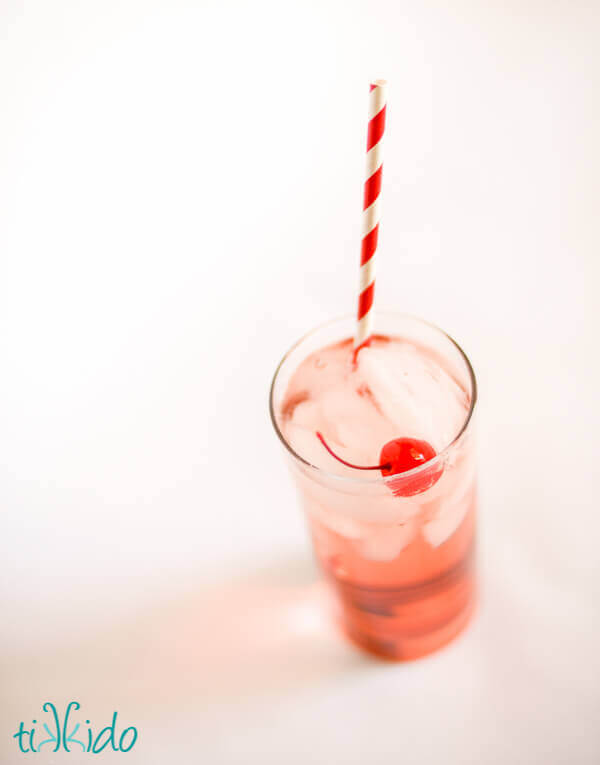 Shirley temple with a maraschino cherry and red and white striped paper straw on a white background.