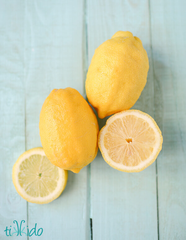 two whole lemons and a third lemon cut in half on a light blue wood background.