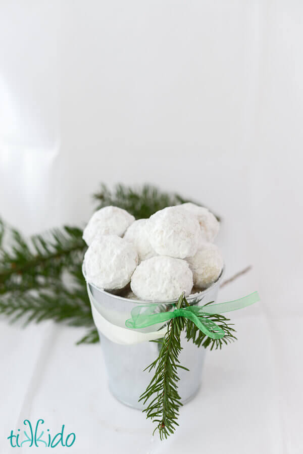 Small silver bucket filled with Russian Tea Cakes cookies and decorated with a sprig of fresh evergreen.