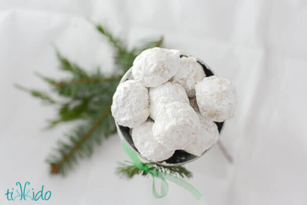 Small silver bucket filled with Russian Tea Cakes cookies and decorated with a sprig of fresh evergreen.
